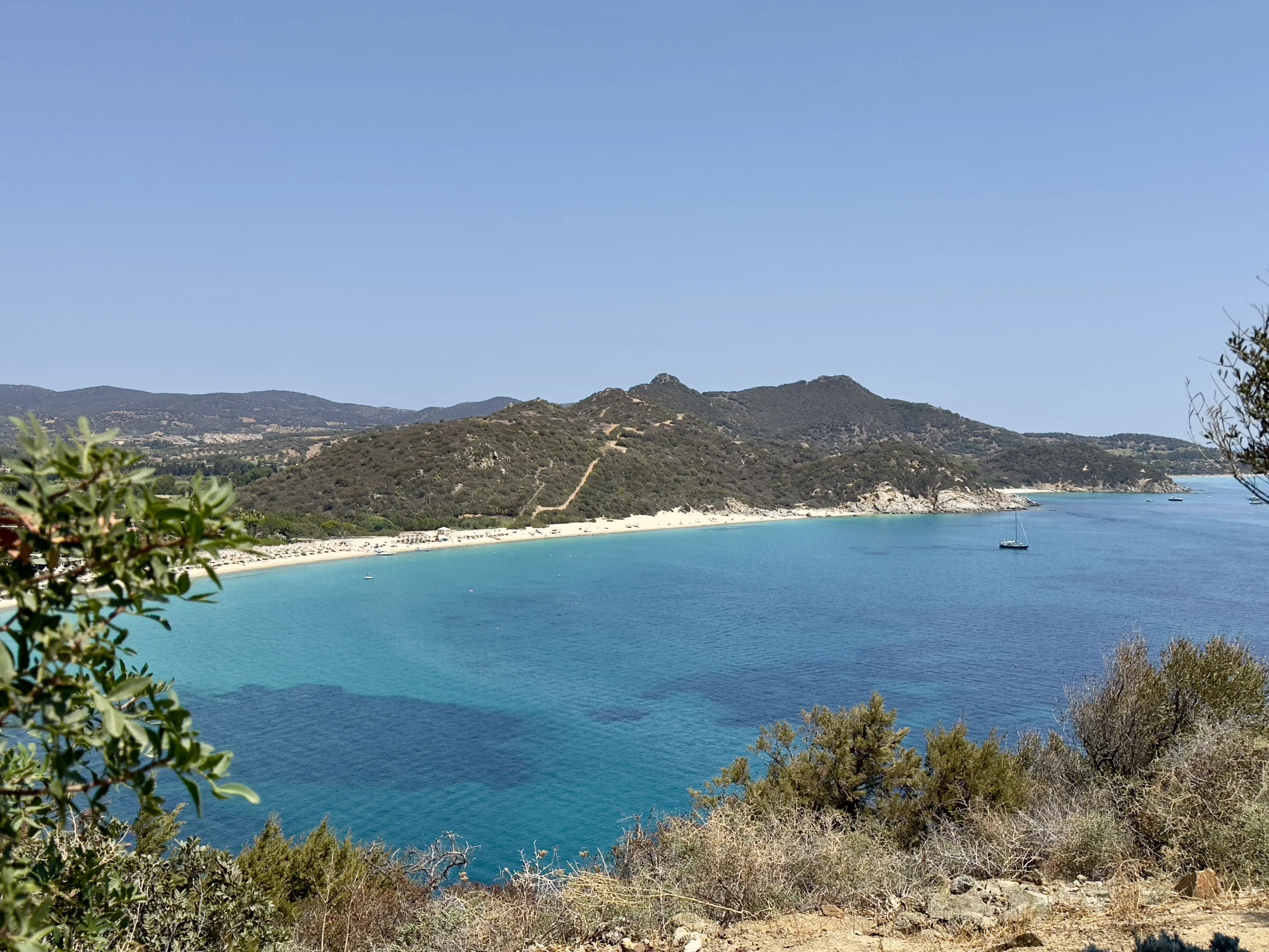 Wide view across a bay in Sardinia with mountains behind