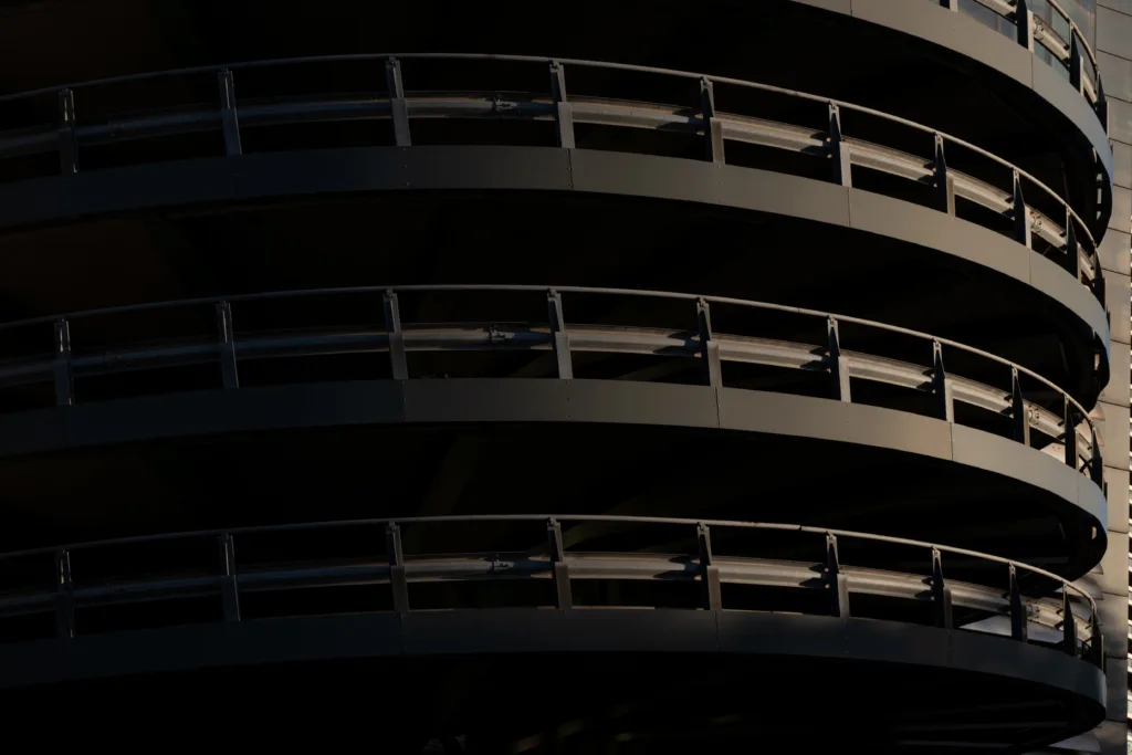 Curved levels of a spiral car park ramp with railings, lit from the side against deep shadow