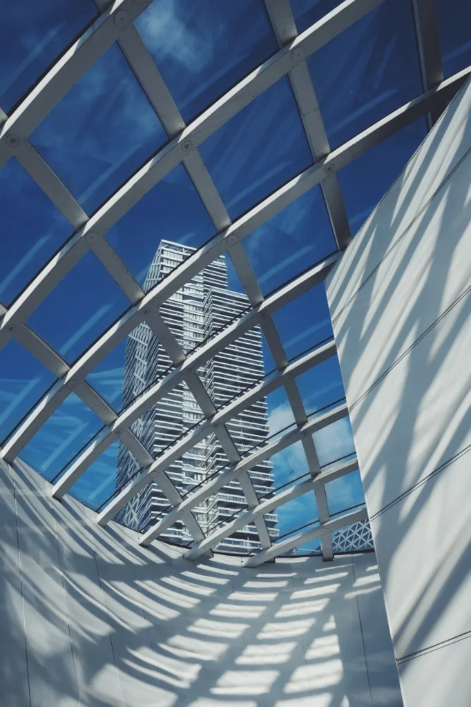 White-framed glass roof with a tower block rising into the blue sky beyond