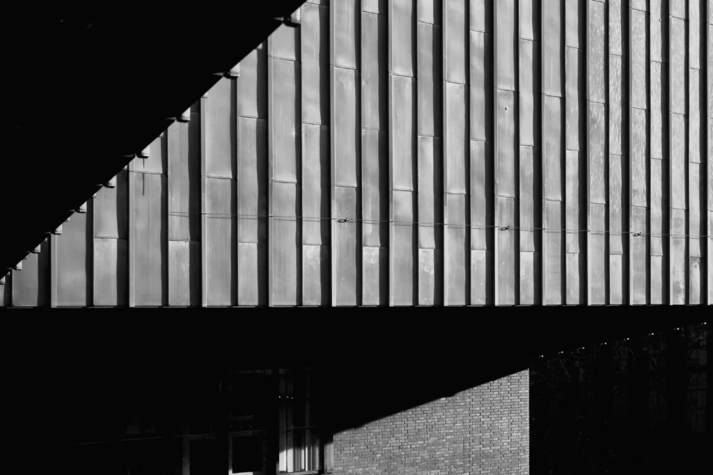 Ribbed concrete facade cut diagonally by a hard shadow, in black and white